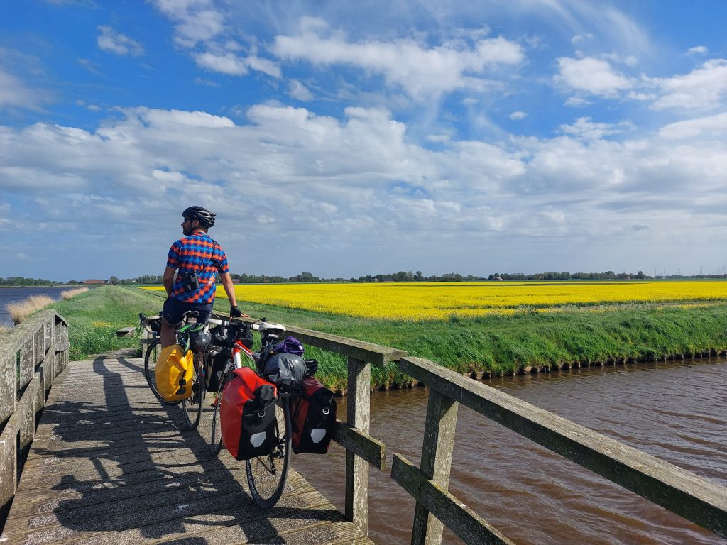 Op de achtergrond een weiland vol koolzaad. Vooraan Barend op een volgeladen racefiets